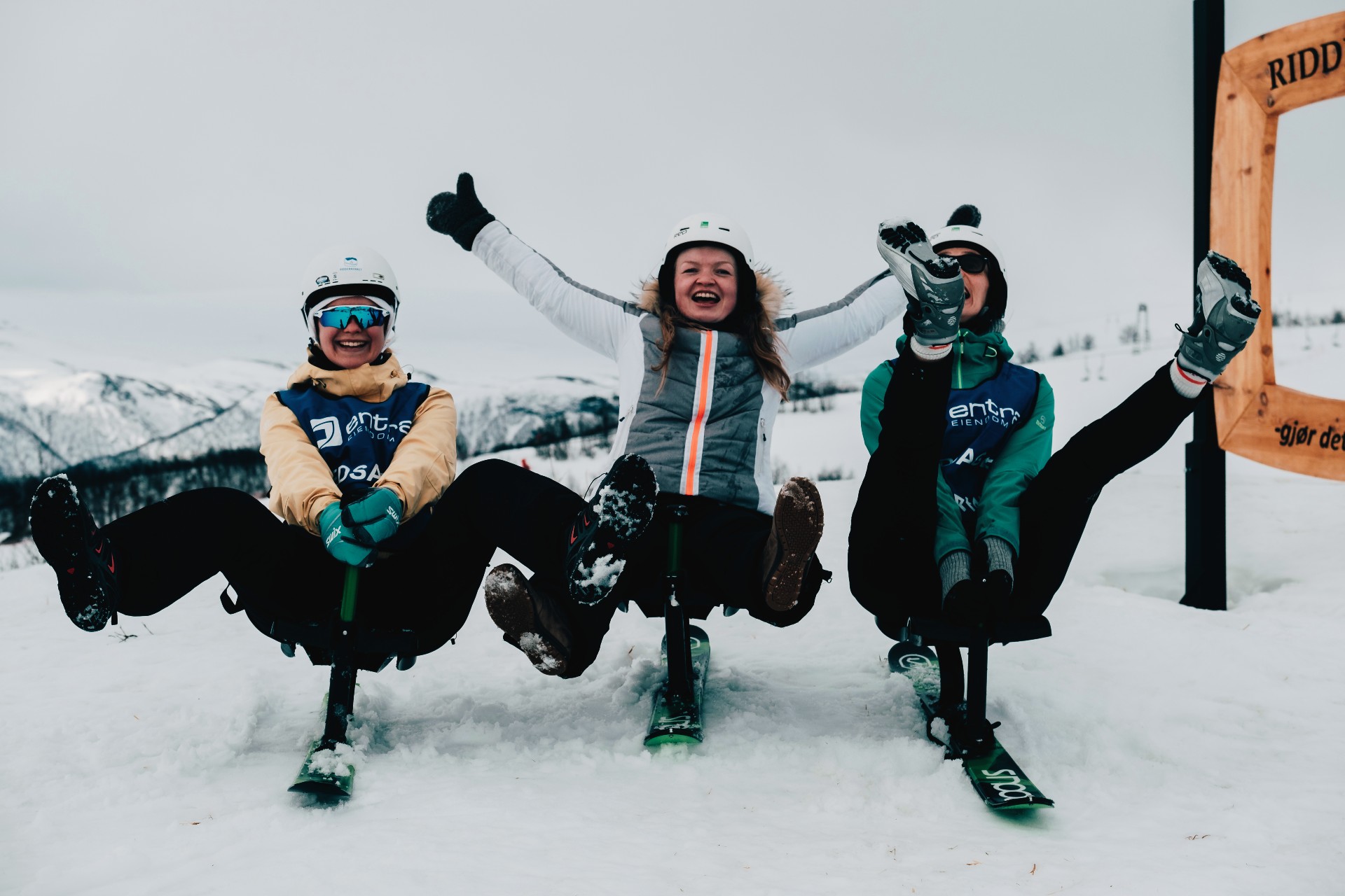 Tre unge mennesker i alpintbakken smiler mot kamera