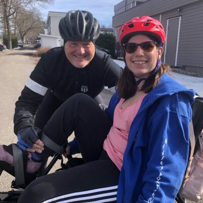 To smilende syklister. En kvinne i en sittesykkel. En mann stående bøyd ved siden av.